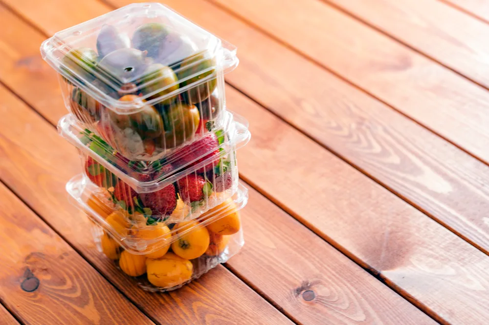 Stacked fresh fruit containers on a wooden table - various PET punnet and clamshell packaging for berries and grapes