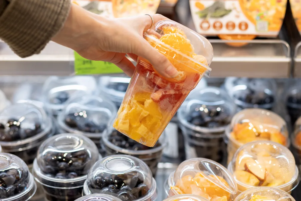 Customer selecting packaged fresh-cut fruit cups from refrigerated retail display