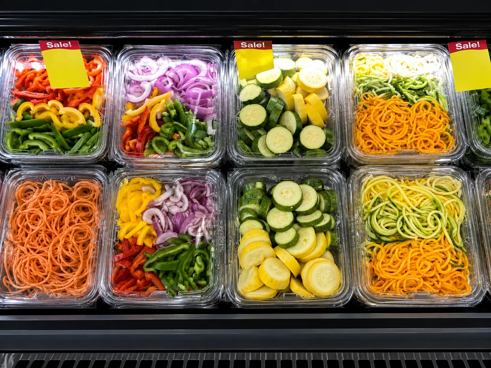 Clear PET tamper-evident food containers displaying fresh-cut vegetables in a refrigerated retail case