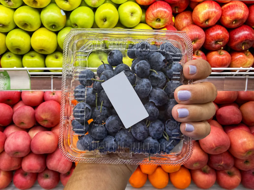 Clear PET plastic grape clamshell container displayed in a supermarket fruit section showing visibility and retail presentation