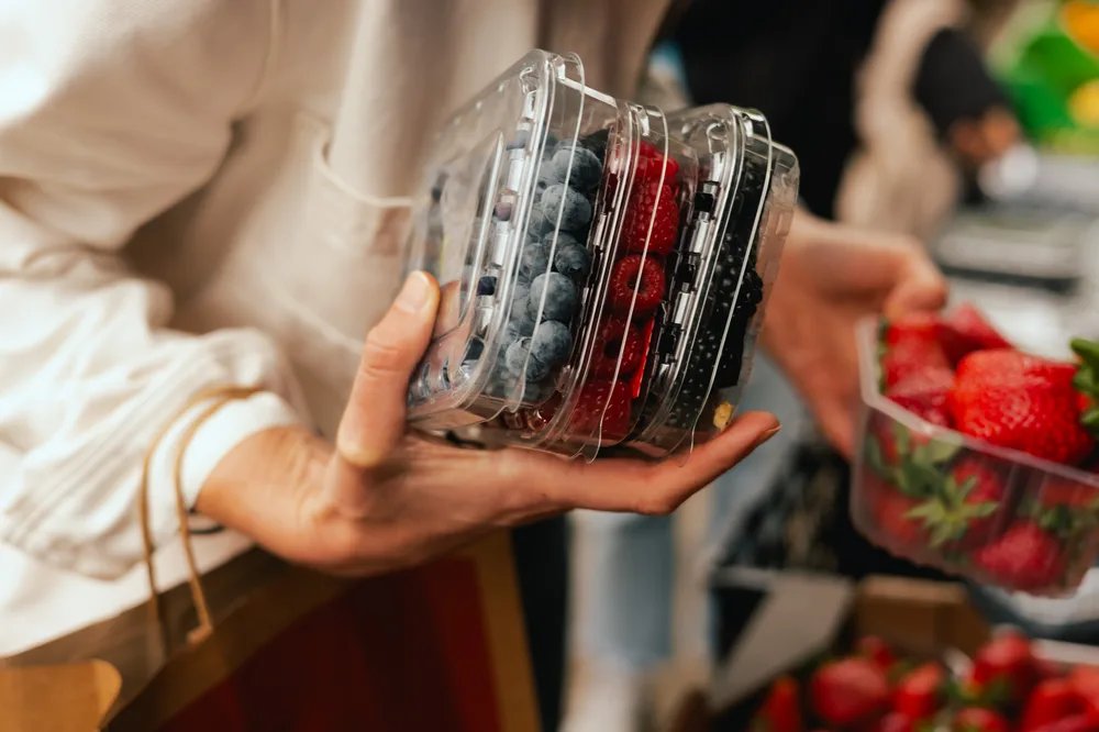 Shopper holding fresh berries in a clear fruit clamshell at a grocery store